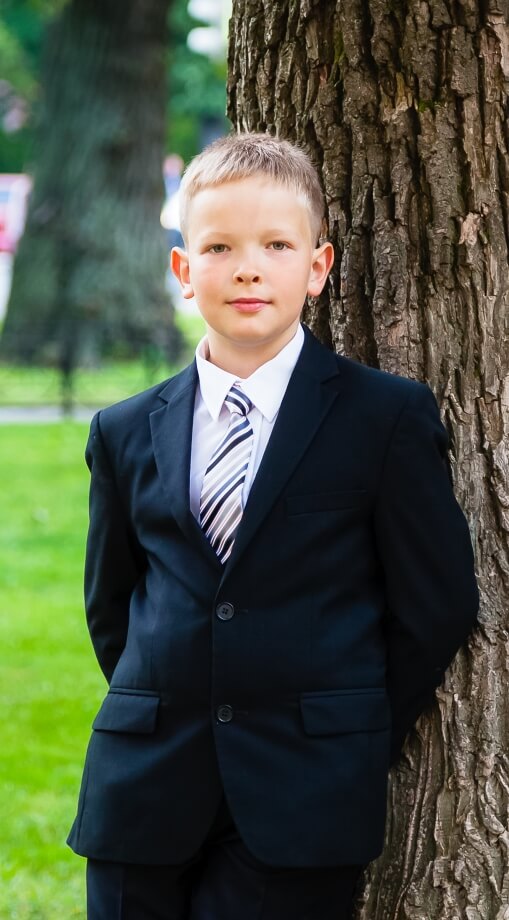 Boy is standing near the school in the city boys navy suit church wedding baptism communion grey brown black white
